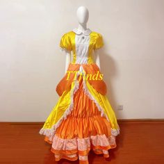 an orange and yellow dress with ruffles on the bottom is sitting on a wooden floor