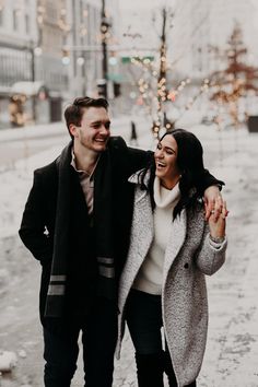 a man and woman walking down the street in the snow with their arms around each other