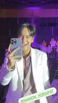 a man in a white suit taking a selfie with his cell phone at an event