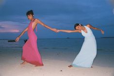 two women in long dresses are dancing on the beach at dusk with their arms around each other