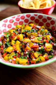 a colorful salad in a bowl next to a bowl of tortilla chips on a wooden table