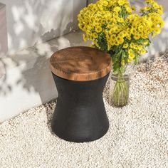 a vase with yellow flowers sitting next to a black stool on the side of a building