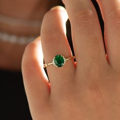 a woman's hand with a green ring on top of her finger and an emerald stone in the middle