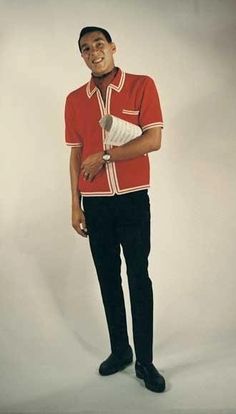 a man standing in front of a white backdrop wearing a red shirt and black pants