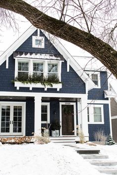 a blue and white house with snow on the ground in front of it's windows