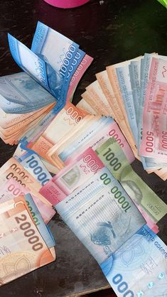 a bunch of mexican currency sitting on top of a black table next to a pink vase