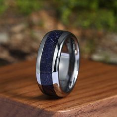 a wedding ring with blue and black inlays on top of a wooden surface