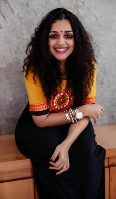 a woman sitting on top of a wooden table wearing a yellow shirt and black pants