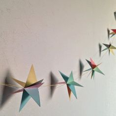 some paper stars are hanging from a string on the wall in front of a white wall