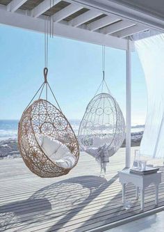 two hanging chairs on a porch next to the ocean