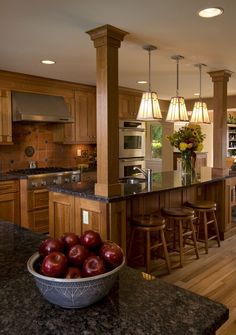 a bowl of apples sits in the middle of a kitchen with an island and bar stools