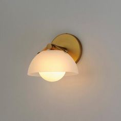 a wall light with a white glass shade on the side and a gold plated arm