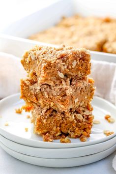 two pieces of carrot cake on a plate with another piece in the background and some oatmeal crumbs on top