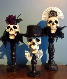 two fake skulls wearing hats and feathers on top of a wooden table in front of a blue wall