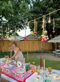 a woman sitting at a table with plates and candles in front of her on the grass