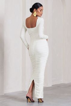 a woman wearing a white dress and high heels standing in front of a wall with her hands on her hips