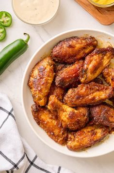 a white bowl filled with chicken wings on top of a table next to green peppers