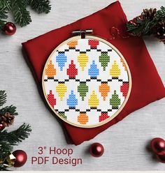 a cross stitch pattern on a red cloth with pine cones and christmas decorations around it