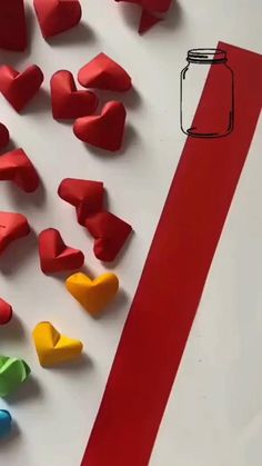 paper hearts next to a red ribbon on a white surface with a mason jar in the background