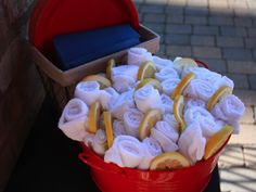 a red bucket filled with lemons and rolls next to a brick wall on a sidewalk