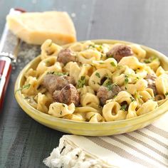 a yellow bowl filled with pasta and meatballs on top of a table next to bread