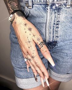 a woman's hand with tattoos on it, and her nails in the shape of stars