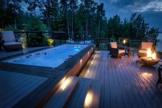 an outdoor hot tub lit up at night on a deck with chairs and fire pit