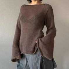 a woman standing in front of a wall wearing a brown sweater and pleated skirt