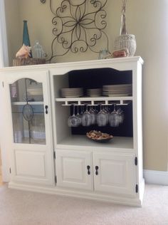 a white china cabinet with dishes and glasses on it