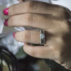 a close up of a person's hand with a ring on their finger and flowers in the background