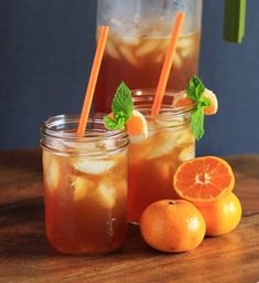 two mason jars filled with iced tea and oranges on a table next to some minty garnishes