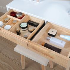 an open drawer with cosmetics and personal care items in it on a wooden floor next to a white table