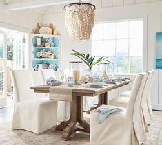 a dining room table with white chairs and a chandelier hanging from the ceiling