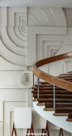 a spiral staircase with wooden handrails in a white walled room next to chairs