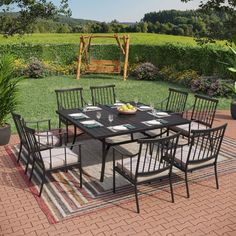 an outdoor dining table with chairs and place settings on a rug in the middle of a yard