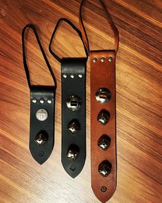 three different types of leather guitar straps on a wooden surface with metal bells attached to them