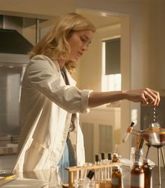 a woman in a white jacket is pouring something into a glass bottle on a counter