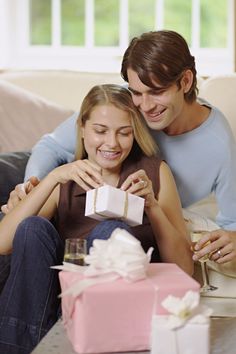 a man and woman sitting on a couch with presents in front of them, smiling