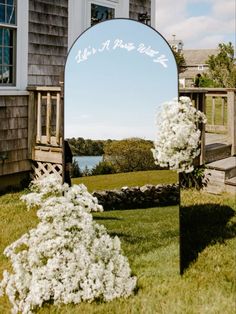 a mirror sitting on top of a grass covered field next to a building and flowers