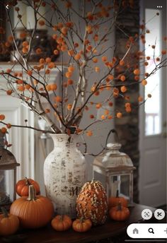 an arrangement of pumpkins and branches in a vase on a table with lantern lanterns