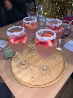 four glasses filled with drinks on top of a wooden table next to a pitcher and glass vase