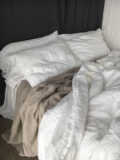 an unmade bed with white sheets and blankets on top of it, next to a black headboard