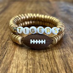 two bracelets with football beads and the word tigers written on them sitting on a wooden table