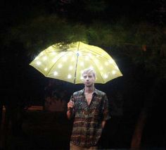 a man holding an umbrella in the dark with lights on his head and shirt off