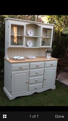 an old china cabinet with plates on it in the grass next to some bushes and trees