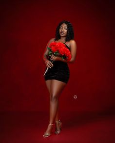 a woman in a short black dress holding red carnations on her left side