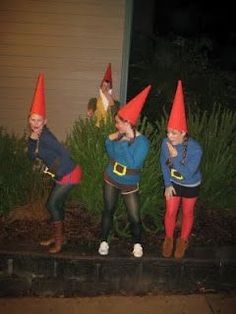 three people dressed as gnomes standing in front of a house at night with their hands on their ears