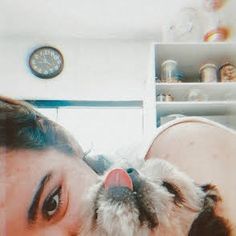 a woman is kissing her dog in front of a clock and shelves with knick knacks