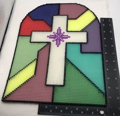 a cross made out of different colored pieces of plastic beads with a ruler next to it