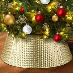 a christmas tree in a basket with lights and ornaments on it's top, sitting on a wooden floor